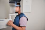 Ein Patient trägt eine Röntgenschürze und steht im digitalen Volumentomographen (DVT) für eine Aufnahme.