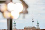 Blick auf den Berliner Fernsehturm und zwei Türme mit grünen Kuppeln, im Vordergrund unscharfe Lichtreflexe.