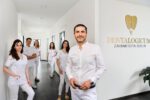 Kamyab Banitorfi und fünf Teammitglieder stehen im Praxisflur vor dem Logo Dentalogicum Zahnmedizin Berlin und posieren für ein Gruppenfoto.