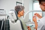 Eine Patientin sitzt im Behandlungsstuhl, während ein Zahnarzt ihr ein Zahnmodell mit eingesetztem Implantat erklärt.