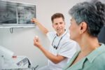 Ein Zahnarzt erklärt einer Patientin anhand von Röntgenbildern auf dem Monitor ein Zahnimplantat.