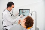 Kamyab Banitorfi zeigt einem Patienten auf einem Bildschirm die Aufnahme eines Kiefers, die mit einem intraoralen Scanner erstellt wurde.