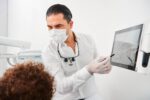 Dr. Kamyab Banitorfi erklärt einem Patienten mithilfe eines Monitors die Ergebnisse einer digitalen Zahnuntersuchung.