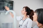 Eine Zahnärztin zeigt einer Patientin auf dem Monitor eine Röntgenaufnahme der Zähne und erklärt die Behandlung.