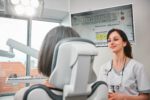 Eine Zahnärztin bespricht mit einer Patientin am Behandlungsstuhl die digitale Auswertung einer Wurzelkanalbehandlung, sichtbar auf dem Monitor.
