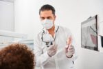 Dr. Kamyab Banitorfi hält einer Patientin eine transparente Zahnschiene und ein Modellzahn vor, um die Behandlung zu erklären.