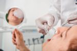 Ein Patient betrachtet sein Lächeln im Spiegel, während eine transparente Zahnschiene vor den Zähnen gehalten wird.