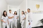 Kamyab Banitorfi und vier Teammitglieder stehen im Praxisflur vor dem Logo Dentalogicum Zahnmedizin Berlin und posieren für ein Gruppenfoto.